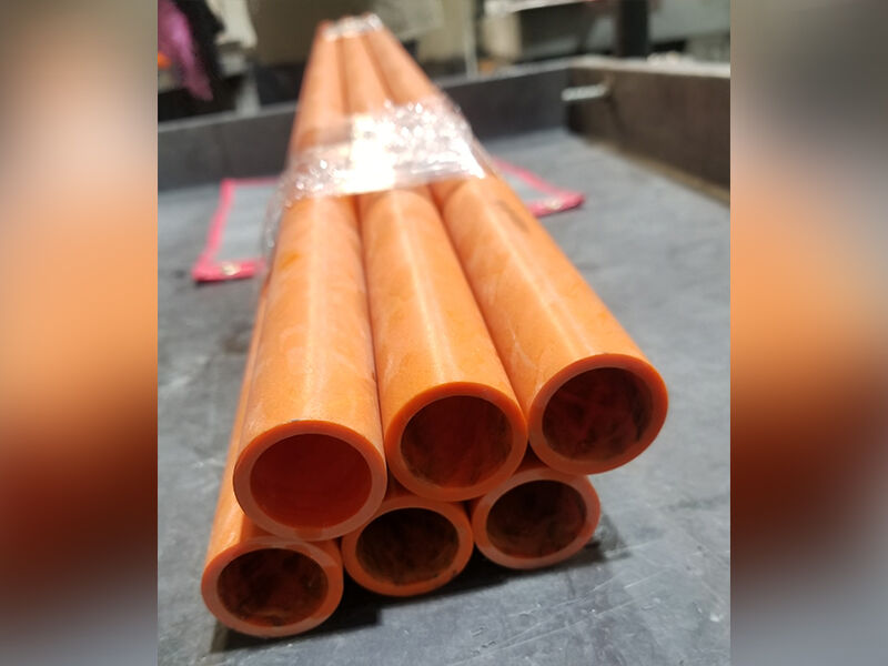 Six orange fiberglass filament wound tubes wrapped with cellophane for transport. Tubes are laying on a grey cart.